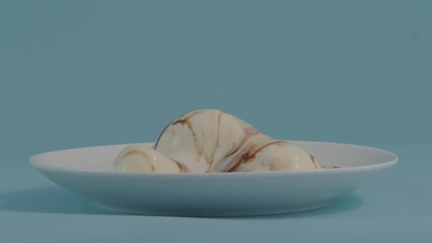 Ice cream with a chocolate topping is melting in a white bowl