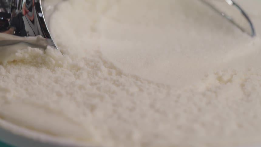 Metal ice cream scoop takes a scoop out of a container of vanilla ice cream