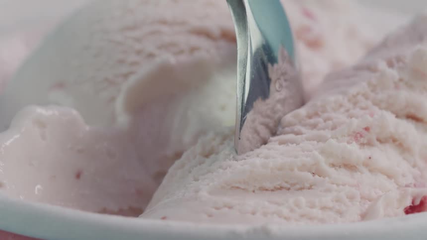 A spoon is put into a tub of strawberry ice cream
