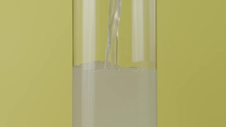 A glass is filled up with a translucent liquid against a yellow background