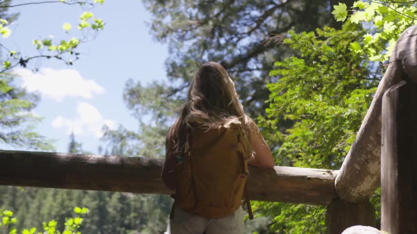 Woman wearing backpack stands near log banister outdoors