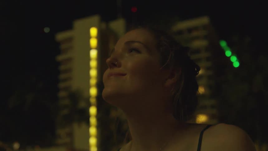 Woman stands outside at night looking up