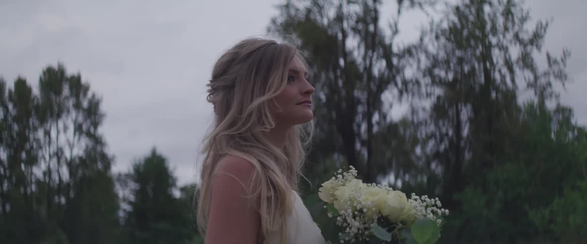A woman stands outside near trees holding a bouquet of flowers