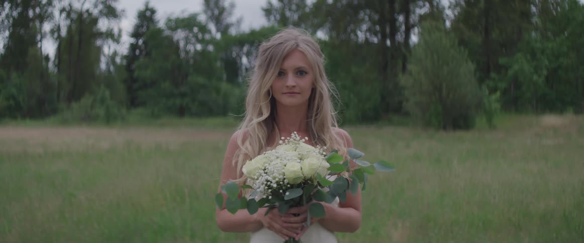 A bride with a flower in her hand stand in the middle of forest