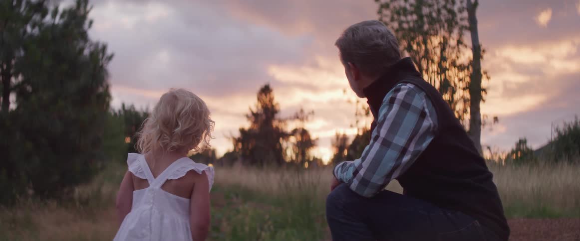 Father and daughter looking at the sunset on a field