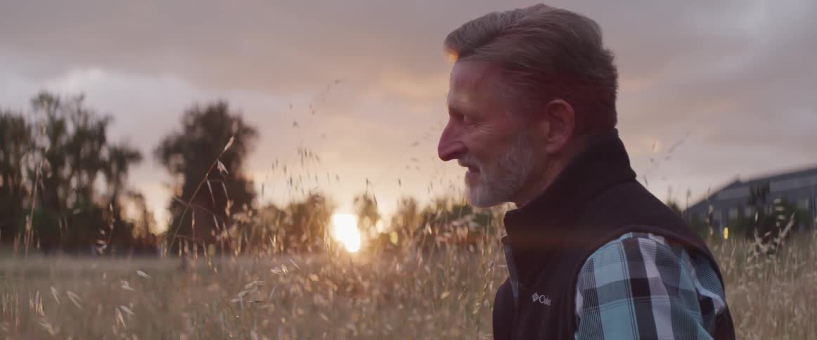 Man stands outdoors in overgrown field as sun rises