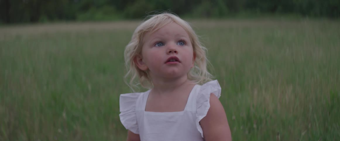Small girl stands in a field of grass and looks at the sky