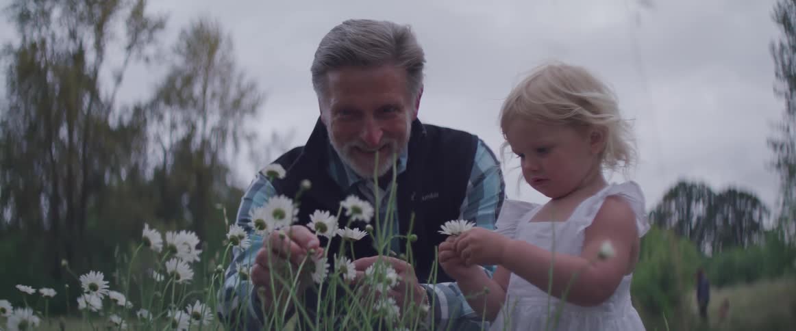 An old man picks daisies with a toddler