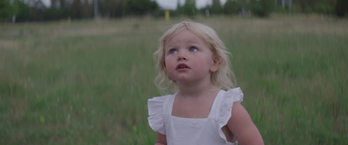 Blonde hair blue eyes toddler girl looks around on the lawn at dusk