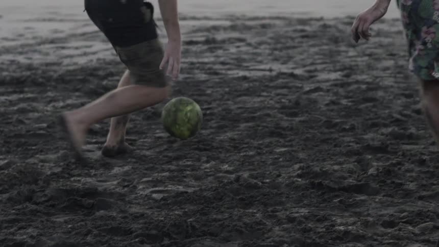 A group plays a casual game of soccer on the beach, kicking the ball across sand near the water.