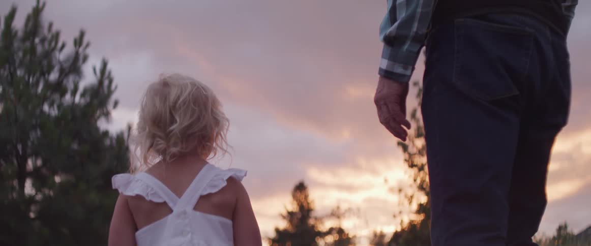 A father and young daughter stand outside at sunset
