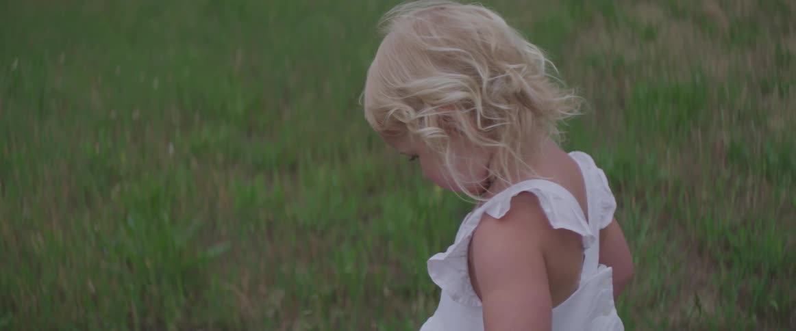 Blonde toddler girl stands on the grass during daylight