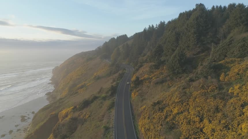 A car travels along a road on a cliff beside a coastline