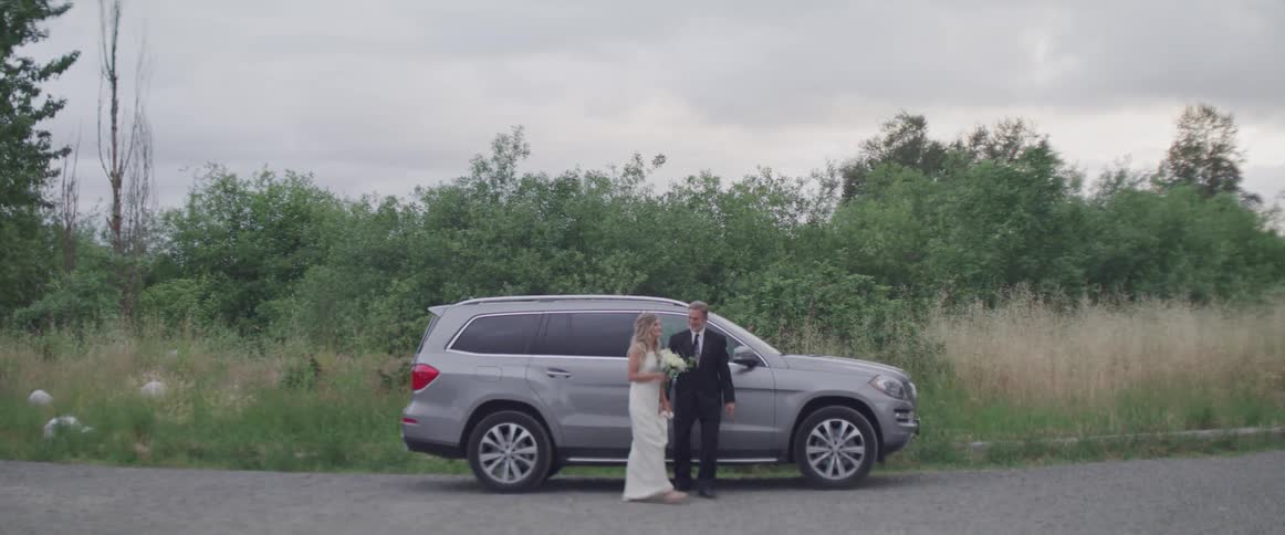 A bride stands beside a car as a man closes the door