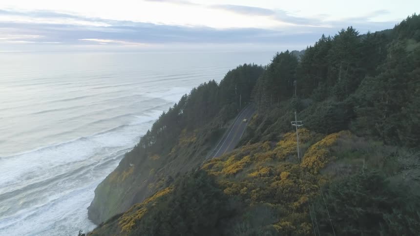 A car drives along a two way road next to a steep cliff
