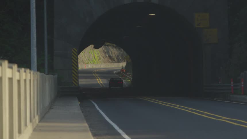 A gray car drives down the road through a dim concrete tunnel