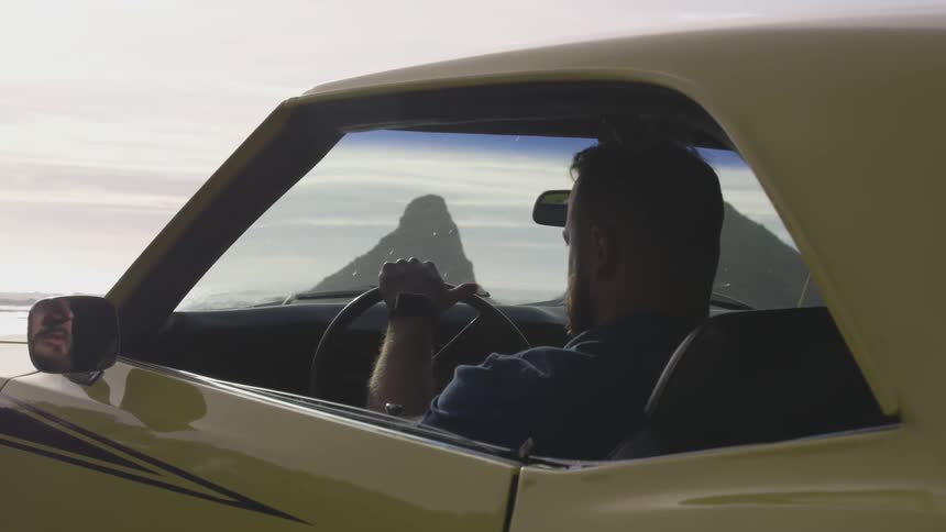 A man is sitting in a yellow sports car with his hand resting on the steering wheel