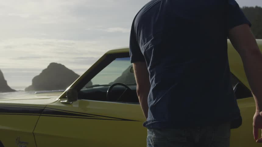 Man walks toward and gets into yellow sports car parked near sea shore
