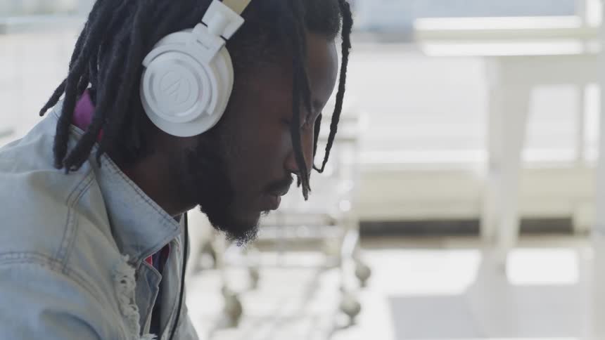 Man with dreadlocks wears headphones as he sits in a room