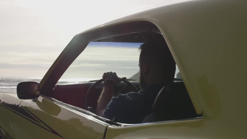 Man sitting at the wheel of a parked car in front of ocean