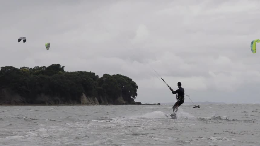 A man holds onto a parasail canopy and skims over the water, performing a thrilling water-boarding ride across the sea.