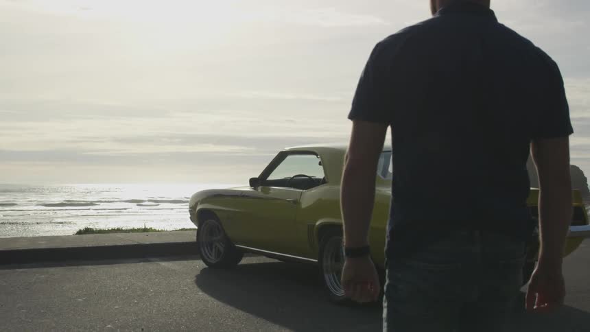 Man walks to the car parked next to the seaside on a sunny day