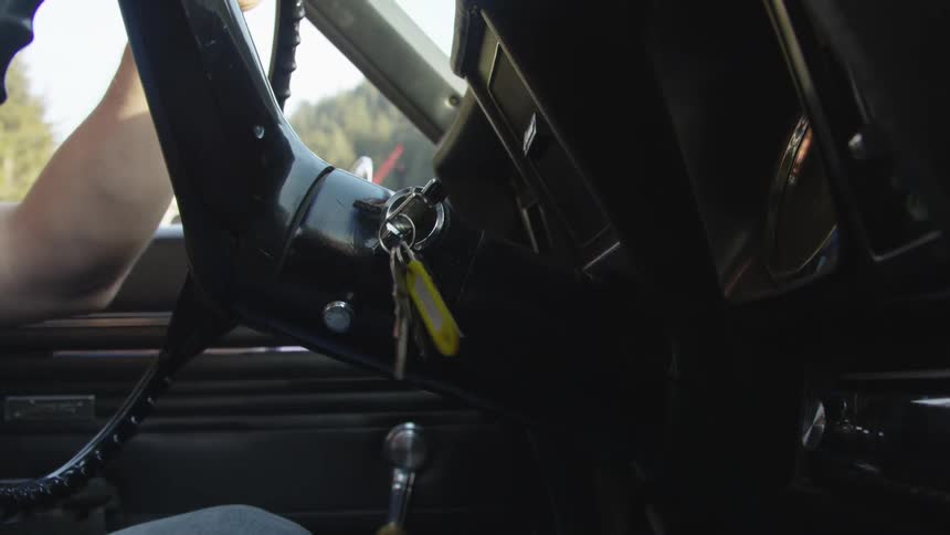 A person turns the key on the ignition in a classic car in daylight