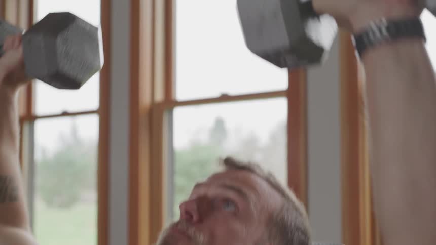 A man indoors lifting silver metal dumbbells