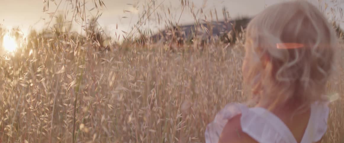 A girl standing in a wheatfield with the sun in the background