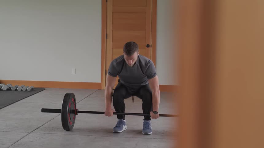 A white male pulls a barbell with a heavy weight on each end up to shoulder height and then sets it back down on the ground