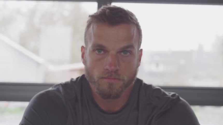 A man sitting with his back to a large window stares straight ahead