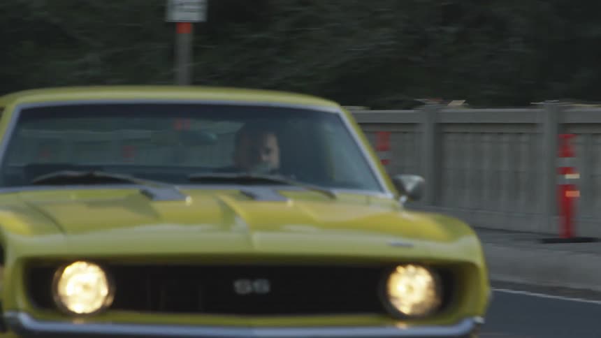 An antique yellow chevy camaro ss driving across a bridge