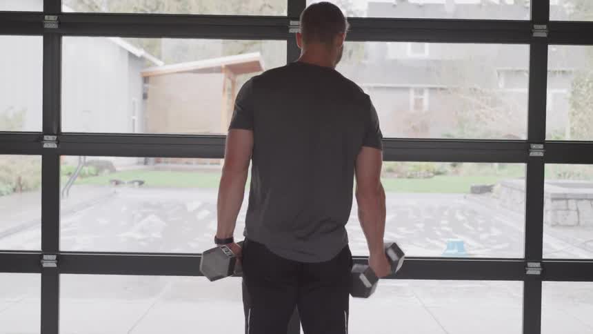 Man lifts dumbbells indoors in front of the window during daylight