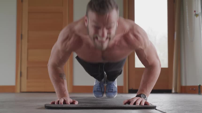 A shirtless man does push ups on a mat in their house