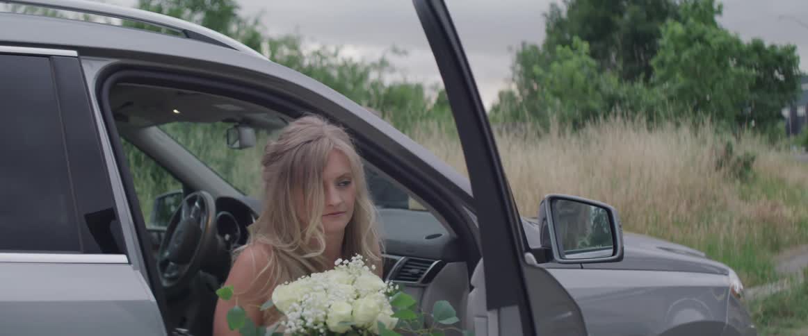 A woman carrying a bouquet of flowers steps out of a car and smiles