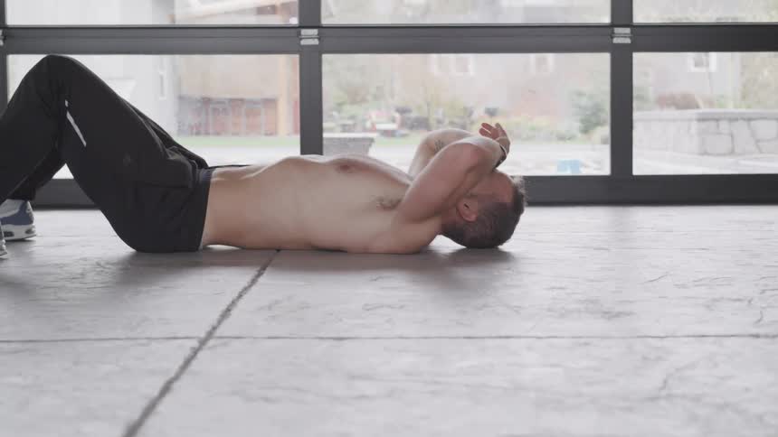 A shirtless man rolls onto the concrete ground on his back