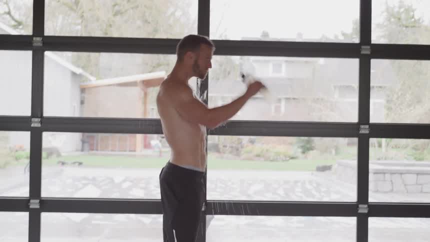 Shirtless man standing in front of a large window cooling down after a workout