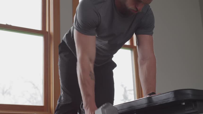 A man kneels on a bench and lifts a weight with his right arm