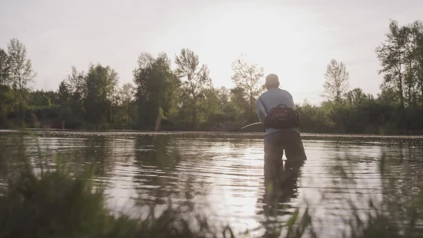 A fisherman casting a fishing line while standing a body of water