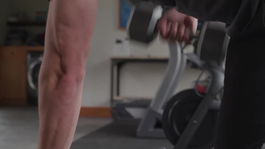 Muscular man lifts dumbbell on bench in gym during daylight