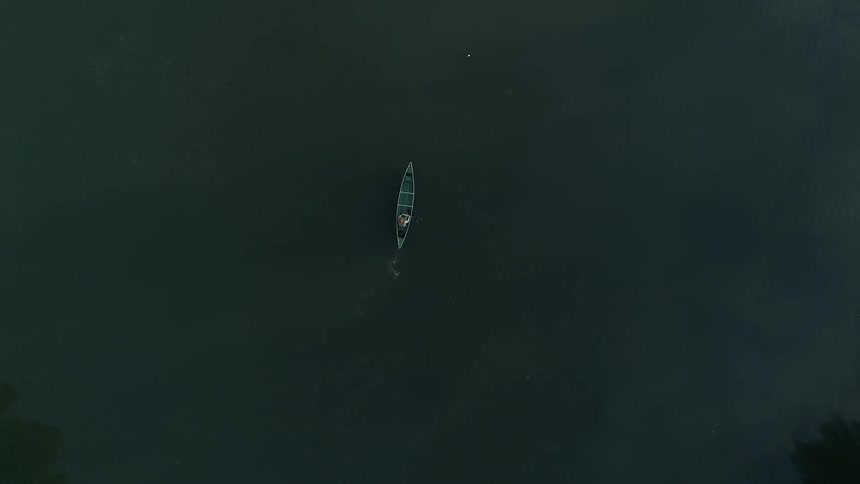 A person paddling a canoe on a lap surrounded by trees