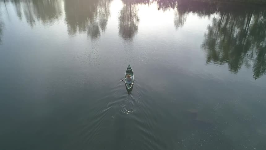 A woman wearing a sun hat paddles a canoe on a calm body of water