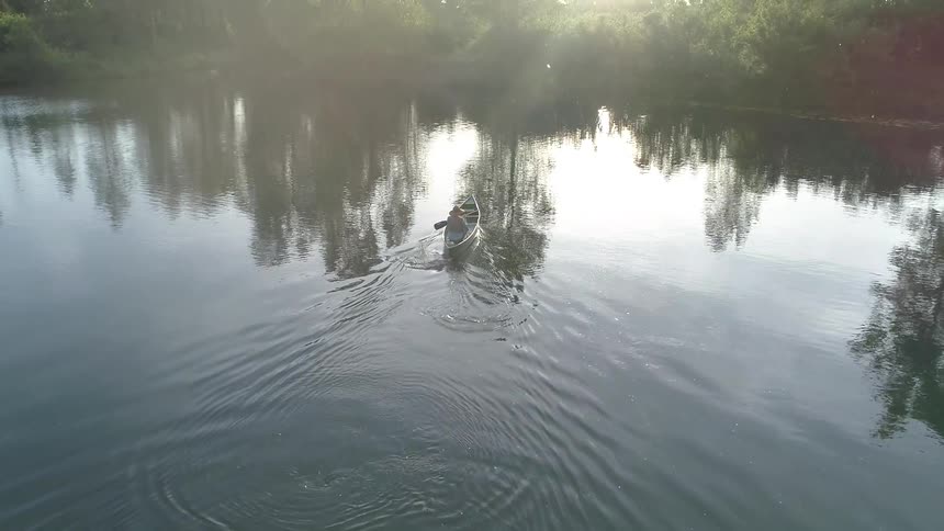 A person paddles a canoe through a calm lake