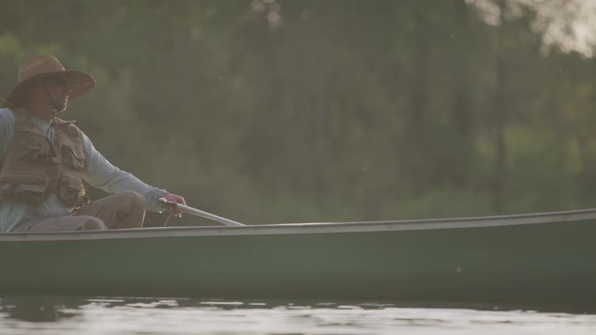 A man sits in a boat fishing and recasts his line