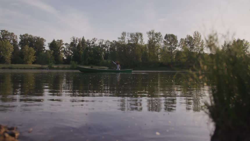 A man sits in a boat fishing in a large pond