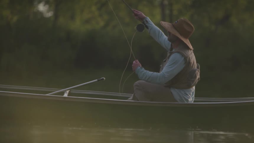 A man in a boat casts his fishing rod in to the lake