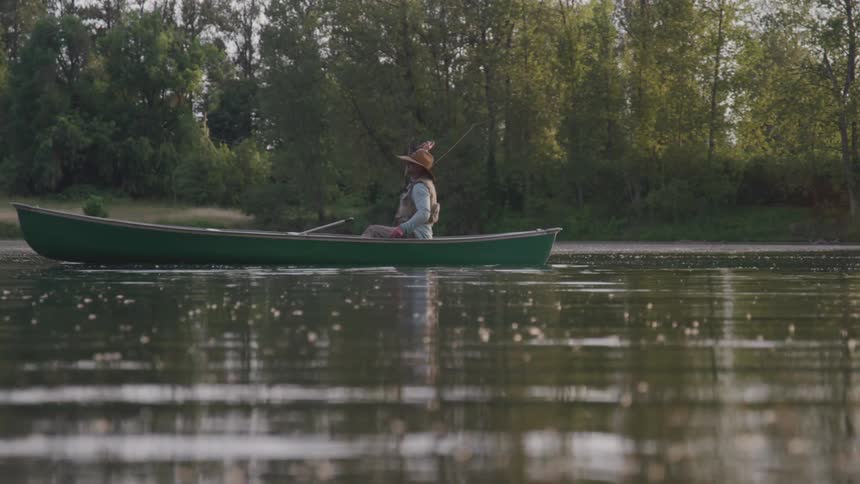 A fisherman sits in a canoe and casts a line into the water