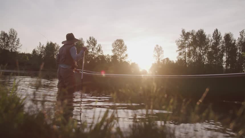 A person stands in water next to a canoe