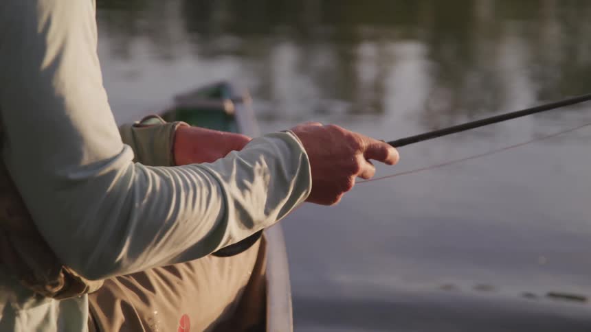 A man sits in a boat and reels his fishing rod in
