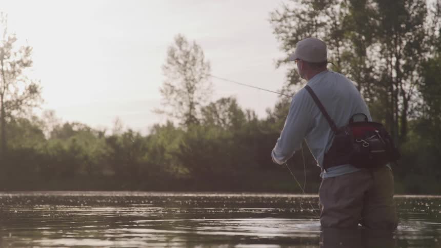A white man stands in water and fly fishes